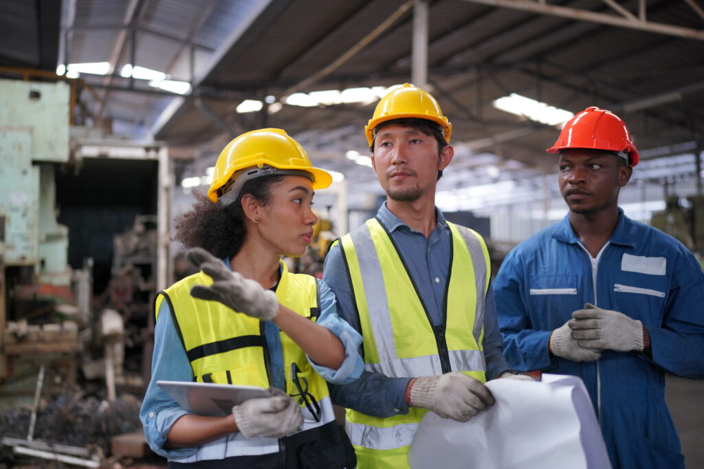 Male and female industrial engineers talk with factory worker against machines and equipments background